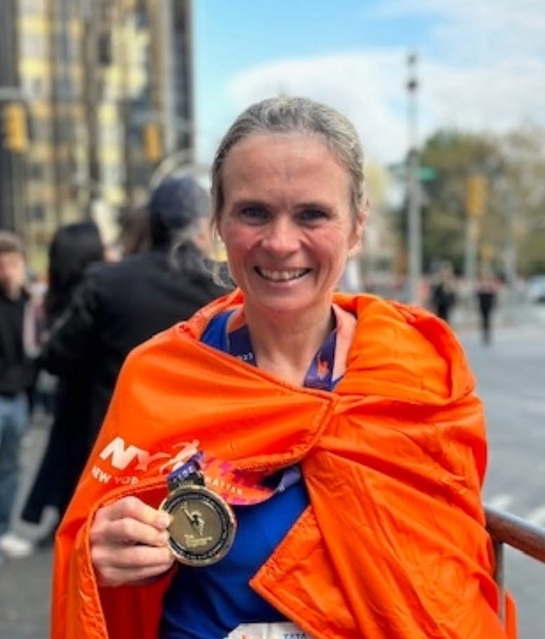 Katya after the New York City Marathon, wrapped in an orange finisher's poncho and holding her medal